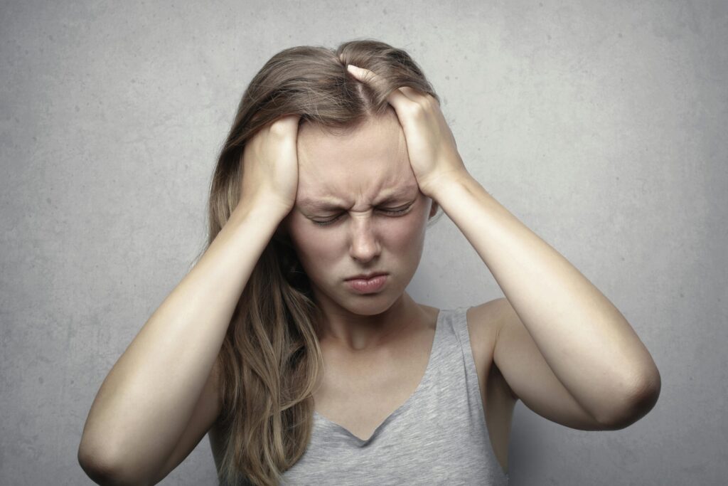 white woman with hands in hair with tension. She's experiencing a headache