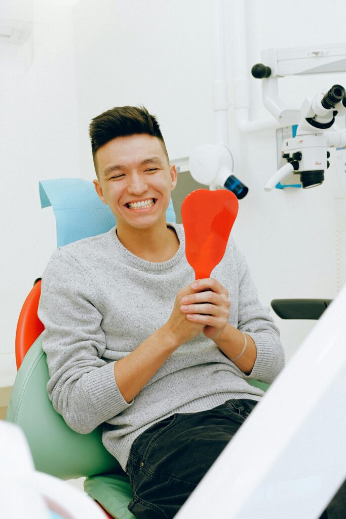 SonderBeaut asian man smiling big looking in a red mirror at the dentist office
